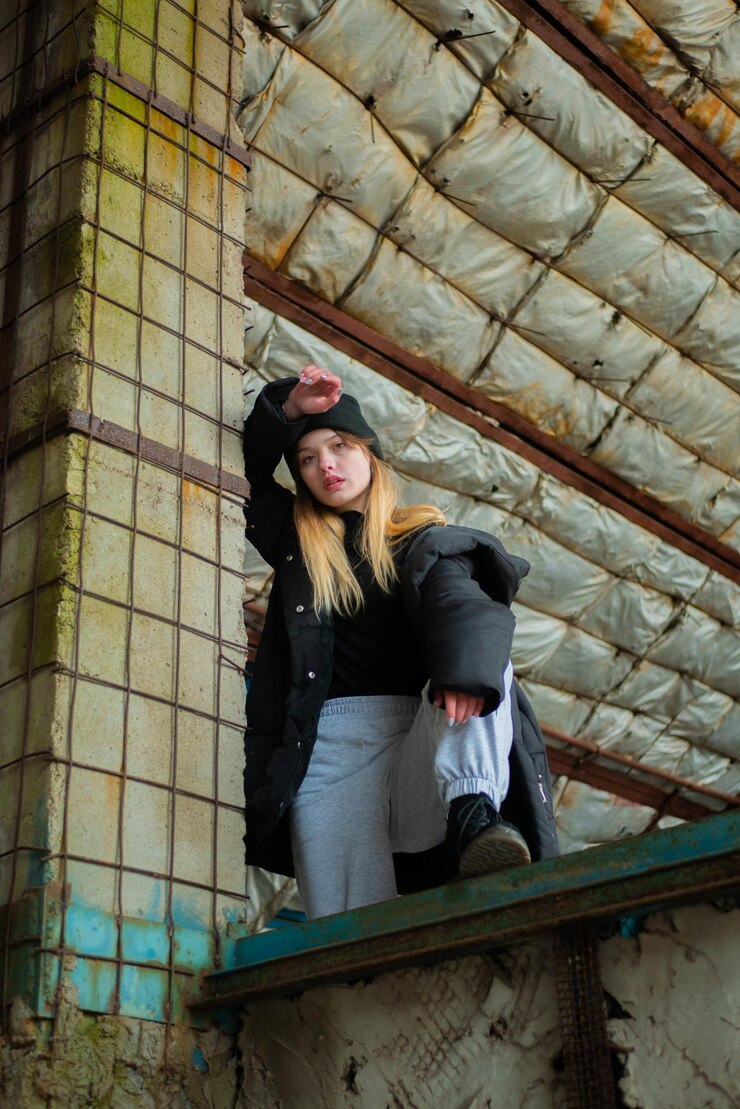 Foto bela adolescente com um casaco de inverno preto e chapéu posa em um edifício destruído e abandonado