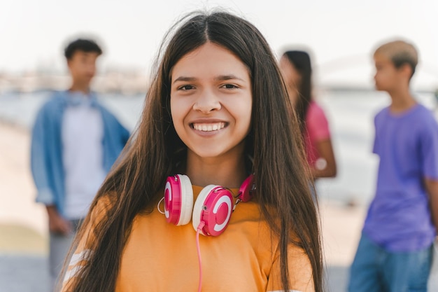 bela adolescente sorridente em camiseta laranja com fones de ouvido olhando para a câmera na rua