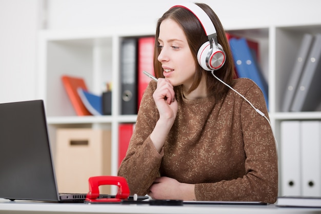 Bela aluna com fones de ouvido, ouvindo música e aprendendo. segure a alça na mão e olhando para o monitor do laptop