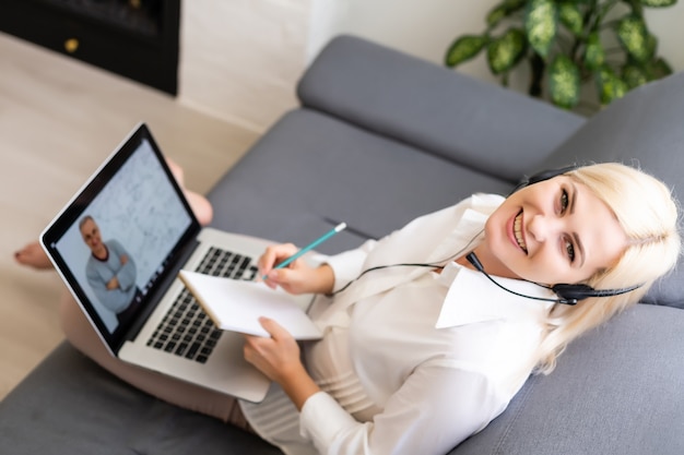 Bela aluna sorridente usando serviço de educação online. Jovem mulher olhando no visor do laptop, assistindo o curso de treinamento e ouvindo-o com fones de ouvido. Conceito moderno de tecnologia de estudo