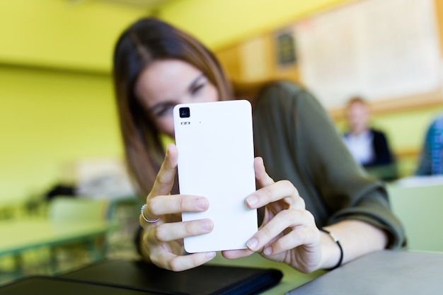 Bela aluna usando seu celular em uma universidade.