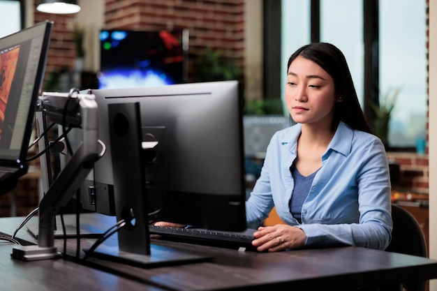 Bela artista criativa asiática sentada na mesa enquanto desenvolve arte digital. Trabalhador de escritório da empresa no departamento de produção trabalhando no computador enquanto projeta gráficos modernos.