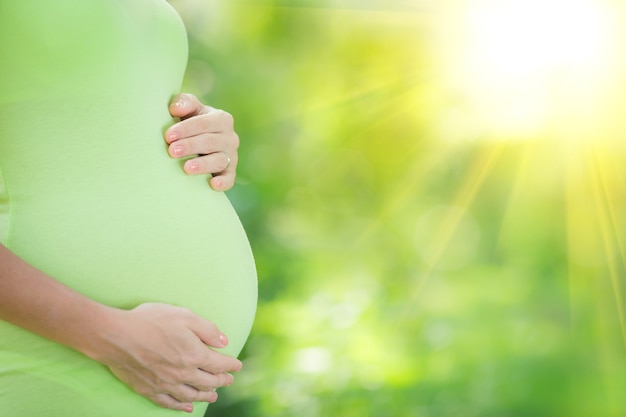 Bela barriga de uma jovem grávida contra um fundo verde primavera