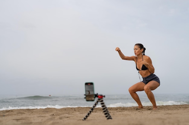 bela blogueira de esportes treina na areia em tira fotos de si mesma em um mobi