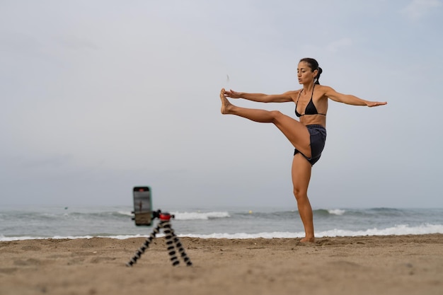 Foto bela blogueira de esportes treina na areia em tira fotos de si mesma em um mobi