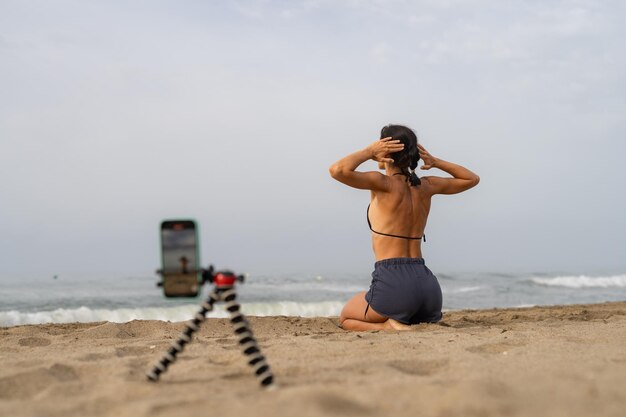 Foto bela blogueira de esportes treina na areia em tira fotos de si mesma em um mobi