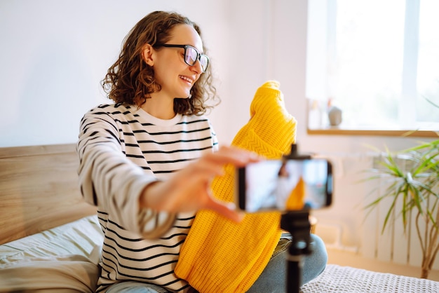 Bela blogueira de moda segurando um suéter amarelo gravando vídeo sonhadoramente para vlog Marketing online