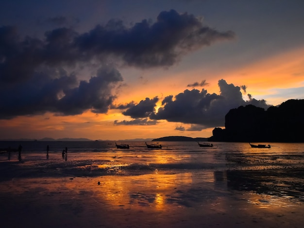 Bela cena do pôr do sol com céu dramático na praia costeira com barcos tradicionais na Tailândia