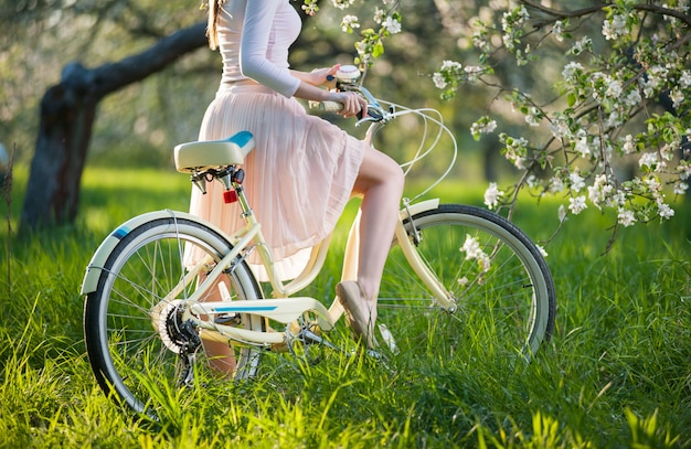 Bela ciclista feminina com bicicleta retrô no jardim primavera