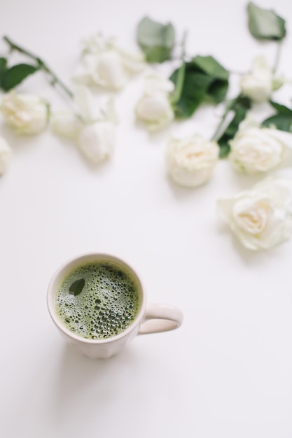 Bela composição com xícara de chá verde matcha e rosas em fundo branco