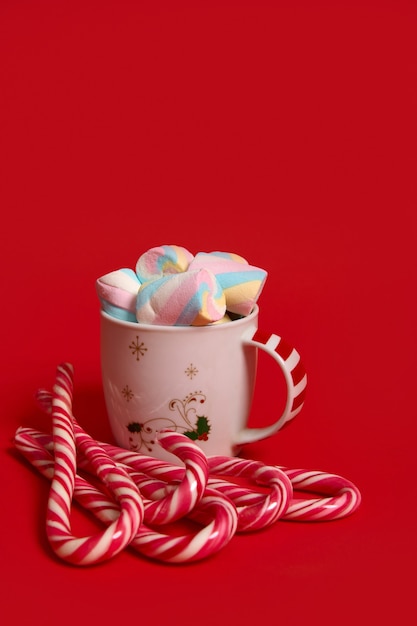 Bela composição minimalista de Natal com bebida de chocolate quente decorada com marshmellows e pirulitos listrados, bastões de doces isolados sobre fundo de cor vermelha com espaço de cópia para publicidade