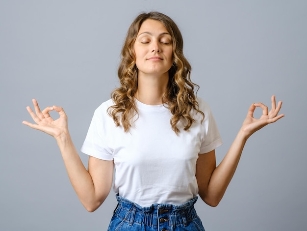 Bela e calma jovem mulher com os olhos fechados enquanto pratica ioga meditando