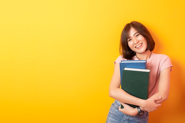 Bela estudante asiática feliz na parede amarela