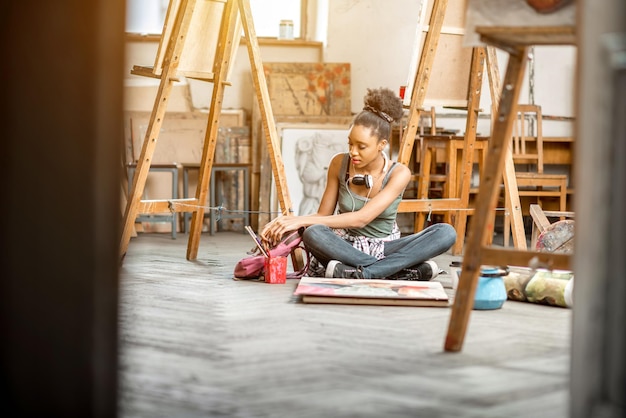 Bela estudante de etnia africana pintando no chão na sala de aula da universidade