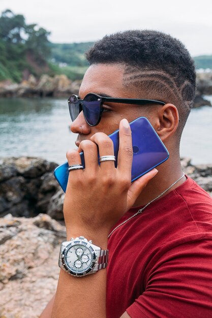 Bela foto de um jovem com óculos de sol falando ao telefone com o lago ao fundo