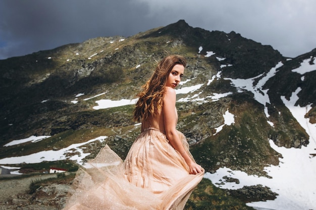 Bela foto de uma mulher caucasiana em um vestido elegante posando em montanhas nevadas