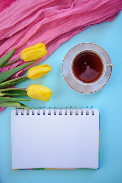 Bela foto romântica com bloco de notas, chá e tulipas em fundo azul