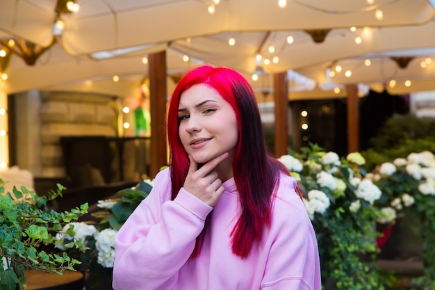 Bela garota ruiva olha com cautela para a câmera à noite em uma rua iluminada da cidade.