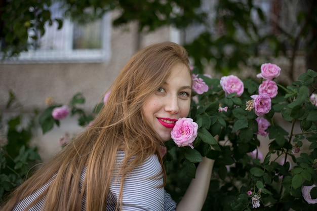 Bela garota ruiva sentada sozinha perto de um arbusto de rosas e sorrindo