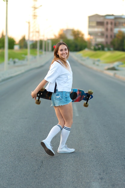 Bela garota sexy em shorts curtos, andando com longboard em tempo ensolarado