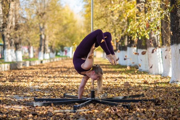 Bela ginasta faz truques em uma plataforma portátil em um lindo parque de outono mulher dança em um palco portátil contra o pano de fundo da queda de folhas de outono Pole dance Uma dança deslumbrante