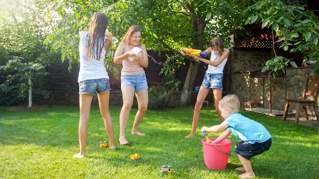 Bela imagem de família feliz rindo com crianças se divertindo em um dia quente de verão com pistolas de água e mangueira de jardim. Família brincando e se divertindo ao ar livre no verão