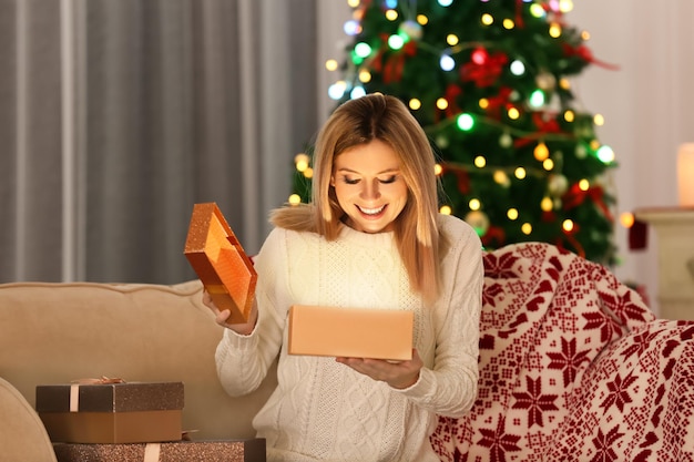 Bela jovem abrindo uma caixa de presente em um quarto decorado para o natal