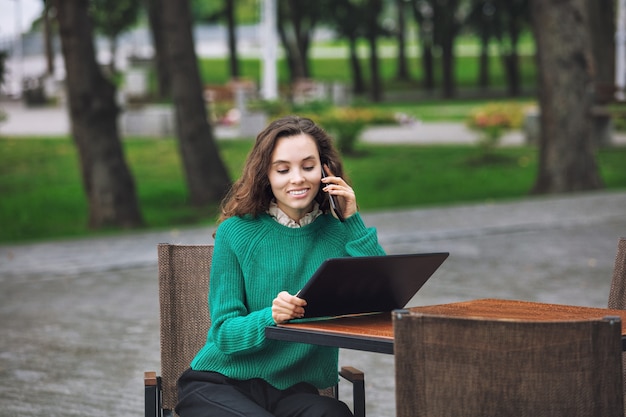 Bela jovem adulta com maquiagem natural na moda com tablet e celular no café de verão