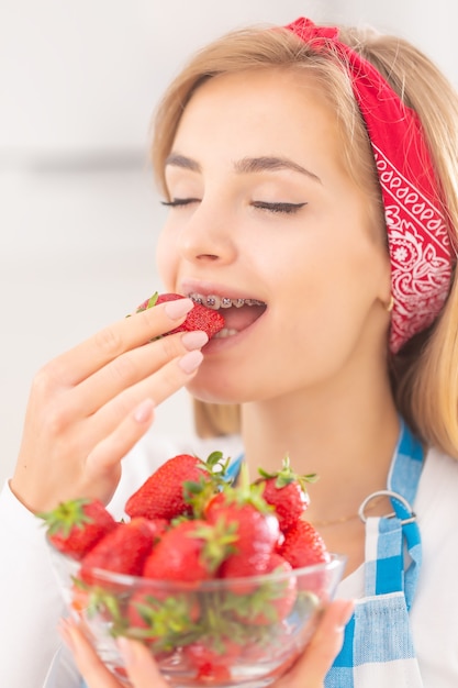 Bela jovem apreciando o sabor de um morango fresco com uma tigela