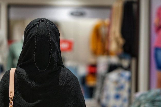 Bela jovem asiática de hijab olhando para produtos de roupa em um centro comercial