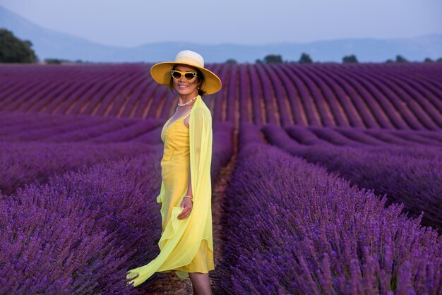 bela jovem asiática em vestido amarelo e chapéu relaxando e se divertindo no campo de lavanda flor roxa