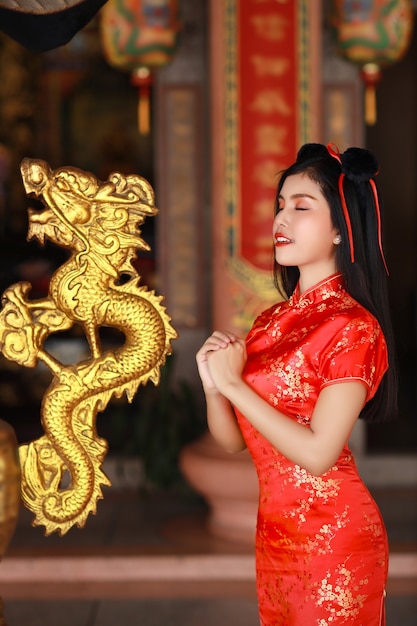 Bela jovem asiática em vestido chinês vermelho tradicional cheongsam qipao com gesto de parabéns e rosto feliz e sorridente