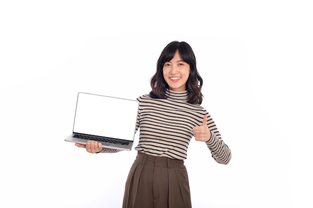 Bela jovem asiática no pano de suéter segurando o computador portátil e olhando para a câmera com o rosto sorridente e o polegar para cima isolado no fundo branco