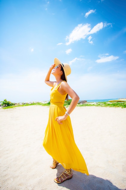 Bela jovem asiática usando vestido amarelo relaxante na praia de vacaiton de verão