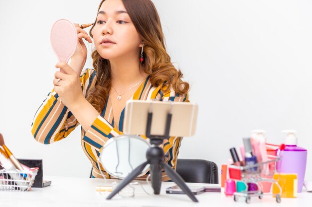 Bela jovem asiática, vlogger, se maquiando enquanto avalia produtos de beleza em um videoblog em casa