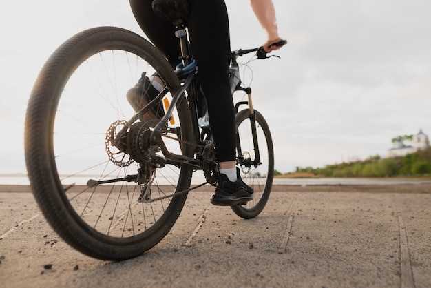 Bela jovem atleta entra para a prática de esportes e anda de bicicleta à beira-mar. perto de um pé feminino no pedal. lugar para texto