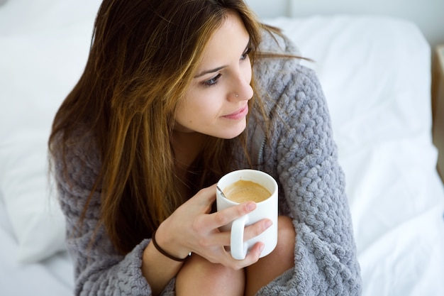 Foto bela jovem bebendo café na cama.