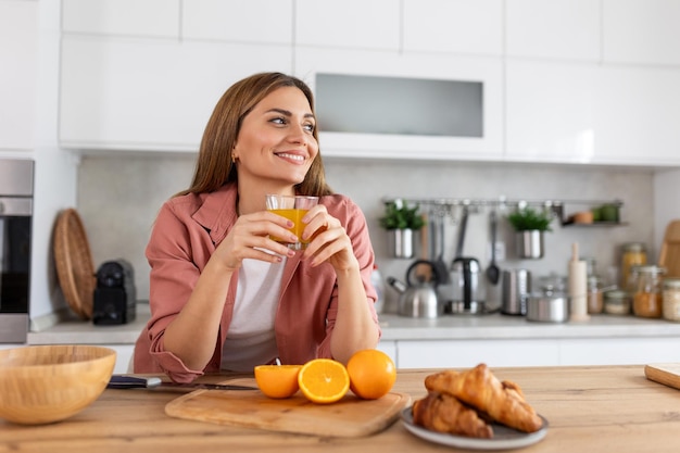 Bela jovem bebendo suco de laranja fresco na cozinha dieta saudável jovem feliz com um copo de suco e laranja na mesa na cozinha