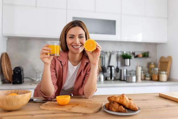 Bela jovem bebendo suco de laranja fresco na cozinha dieta saudável jovem feliz com um copo de suco e laranja na mesa na cozinha