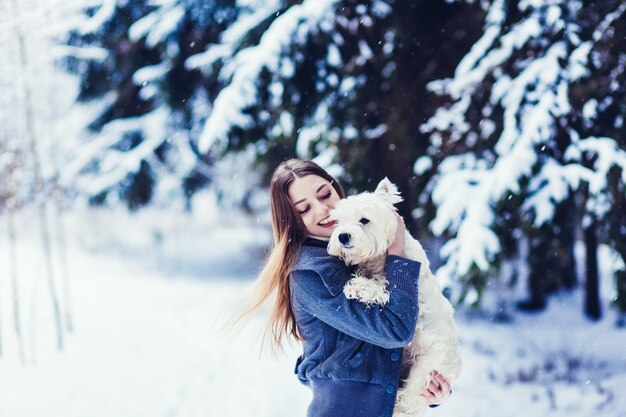 Bela jovem brincando com seu cachorro branco em um parque de inverno. Dia adorável de neve.