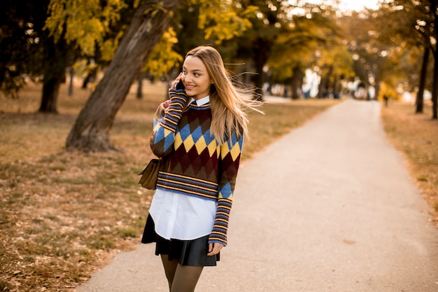 Bela jovem caminhando no parque outono e usando um telefone celular