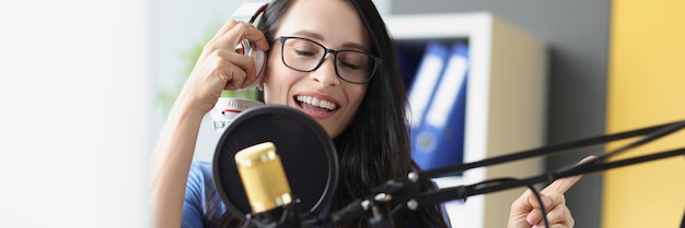 Bela jovem cantando no microfone com fones de ouvido gravando uma música em estúdio