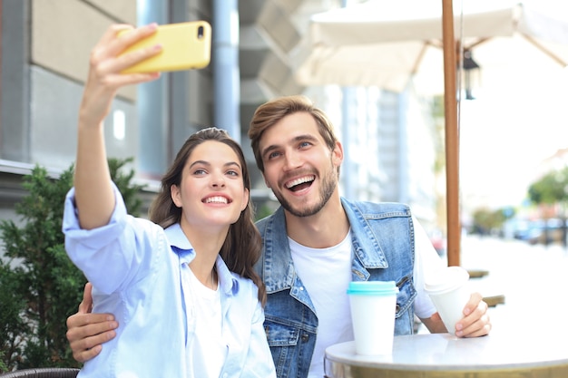 Bela jovem casal apaixonado se unindo no café enquanto mulher fazendo selfie por telefone inteligente.