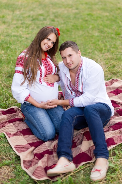 Bela jovem casal grávida vestida em estilo ucraniano nacional fazendo piquenique no parque outono. Maternidade e o conceito de felicidade familiar.