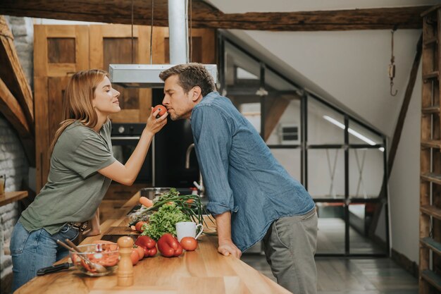 Foto bela jovem casal sorrindo enquanto cozinhando na cozinha em casa