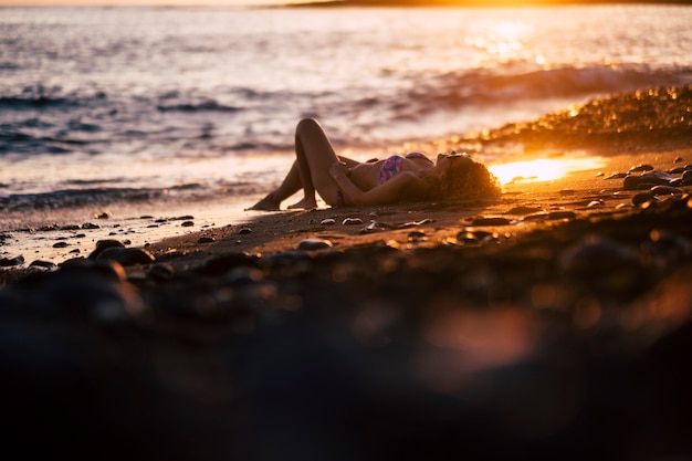 bela jovem caucasiana tomar sol e relaxar na praia durante o pôr do sol no final de um dia de férias. atividade ao ar livre da natureza do oceano para uma linda senhora curtindo o estilo de vida perto do oceano