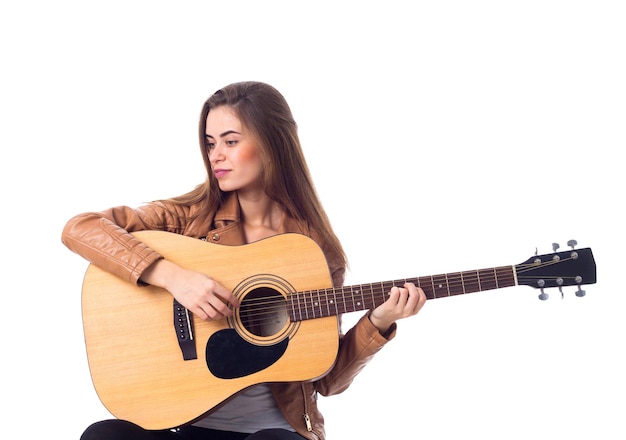 Bela jovem com cabelo comprido na jaqueta marrom tocando guitarra em fundo branco no estúdio