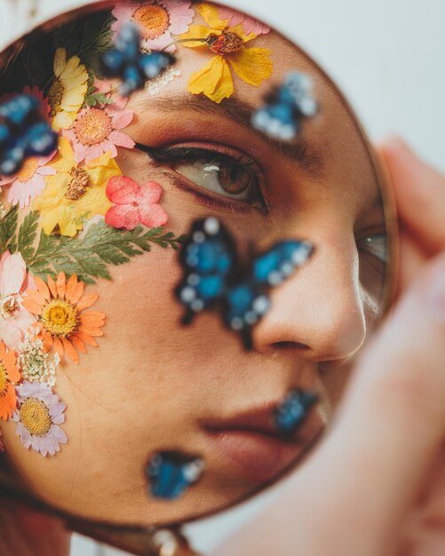 Foto bela jovem com flores no rosto visto no espelho