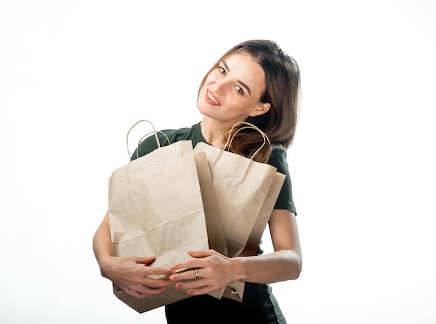 Bela jovem com sacolas de papel. Fundo branco. Senhora sorridente feliz abraçando sacos de papel pardo.