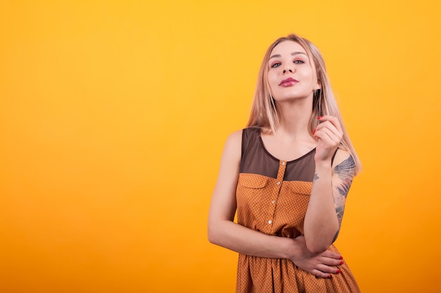 Bela jovem com tatuagem na mão em vestido casual sobre fundo amarelo. Cabelo comprido lindo. Mulher jovem e alegre.